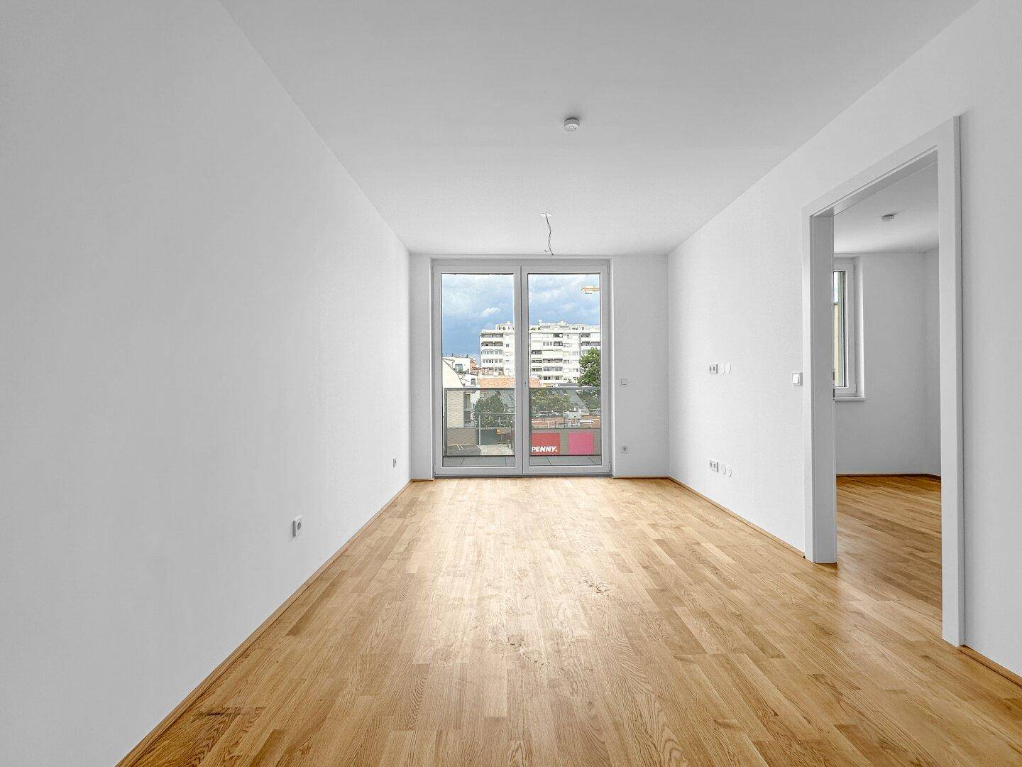 Geräumiges Wohnzimmer mit Holzboden und Zugang zu einem Balkon, bietet viel Tageslicht.