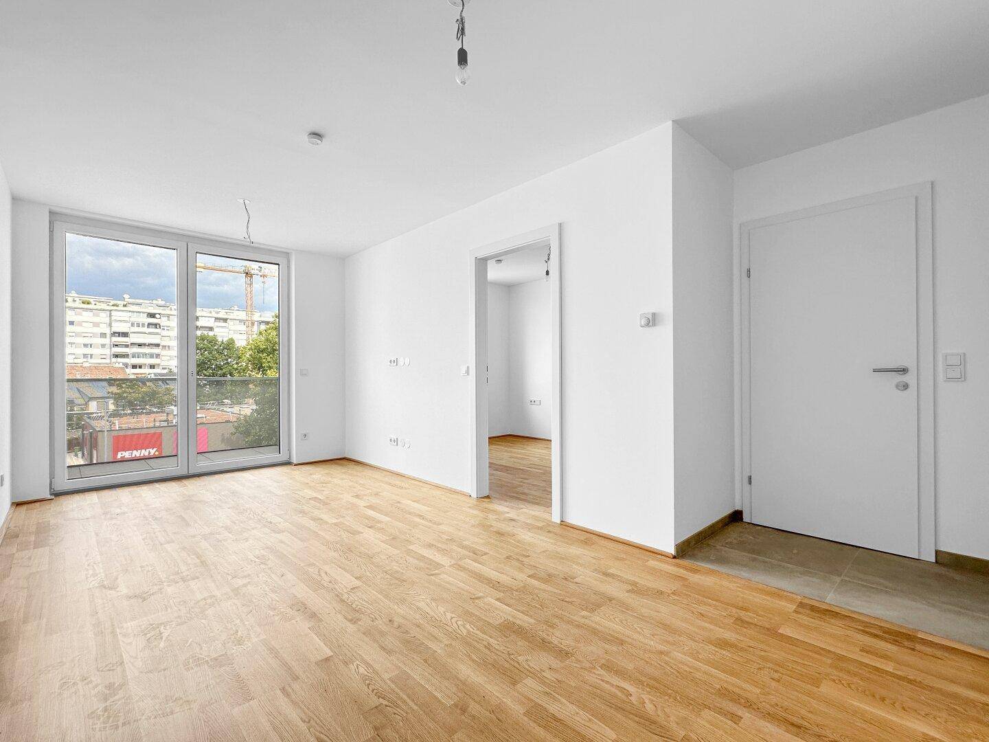 Heller Wohnbereich mit Parkettboden, Balkonzugang und Blick auf die städtische Umgebung.