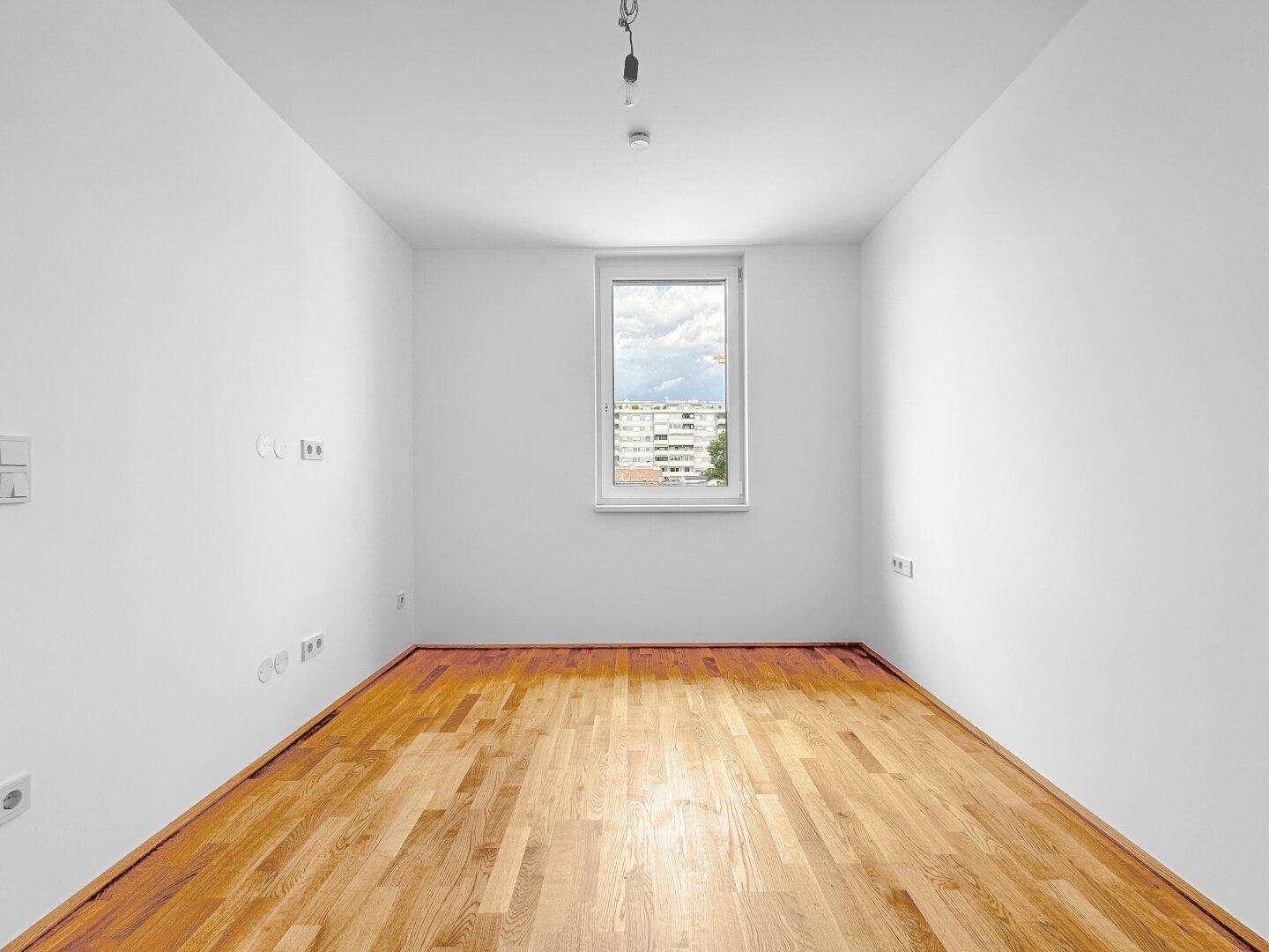 Ruhiges Zimmer mit Holzboden und einem Fenster, das viel natürliches Licht hereinlässt.