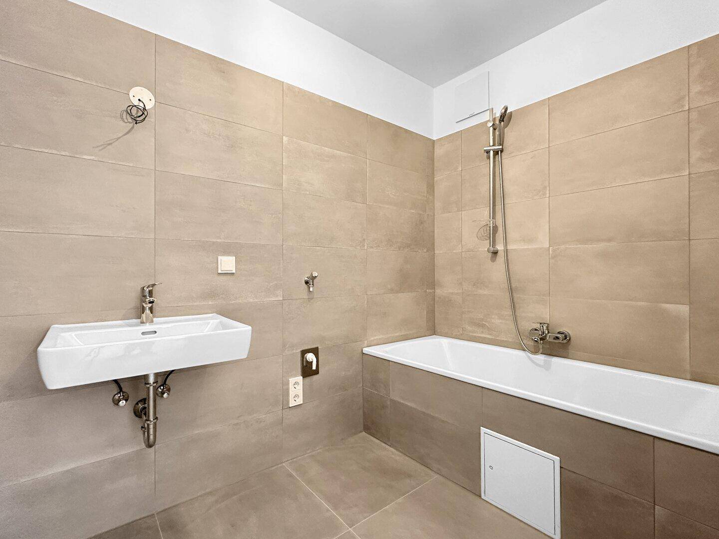 Modernes Badezimmer mit Badewanne, Waschbecken und beigefarbenen Fliesen an Wänden und Boden.