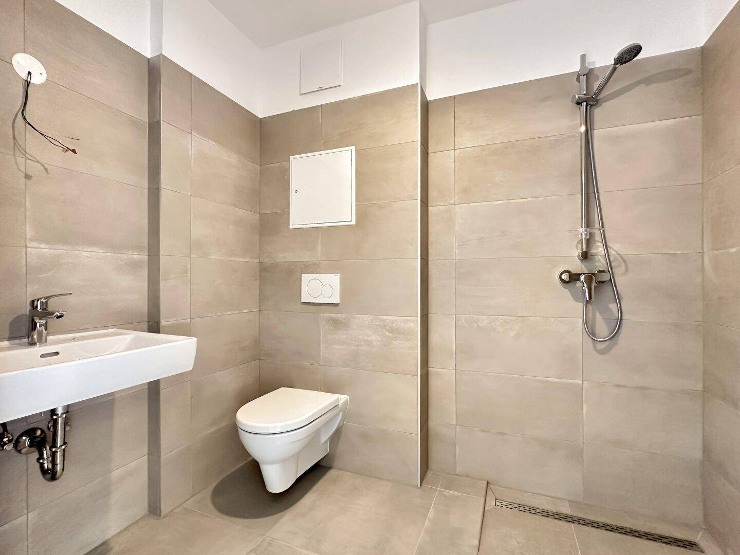 Modernes Badezimmer mit beigefarbenen Fliesen, wandhängendem WC und ebenerdiger Dusche.