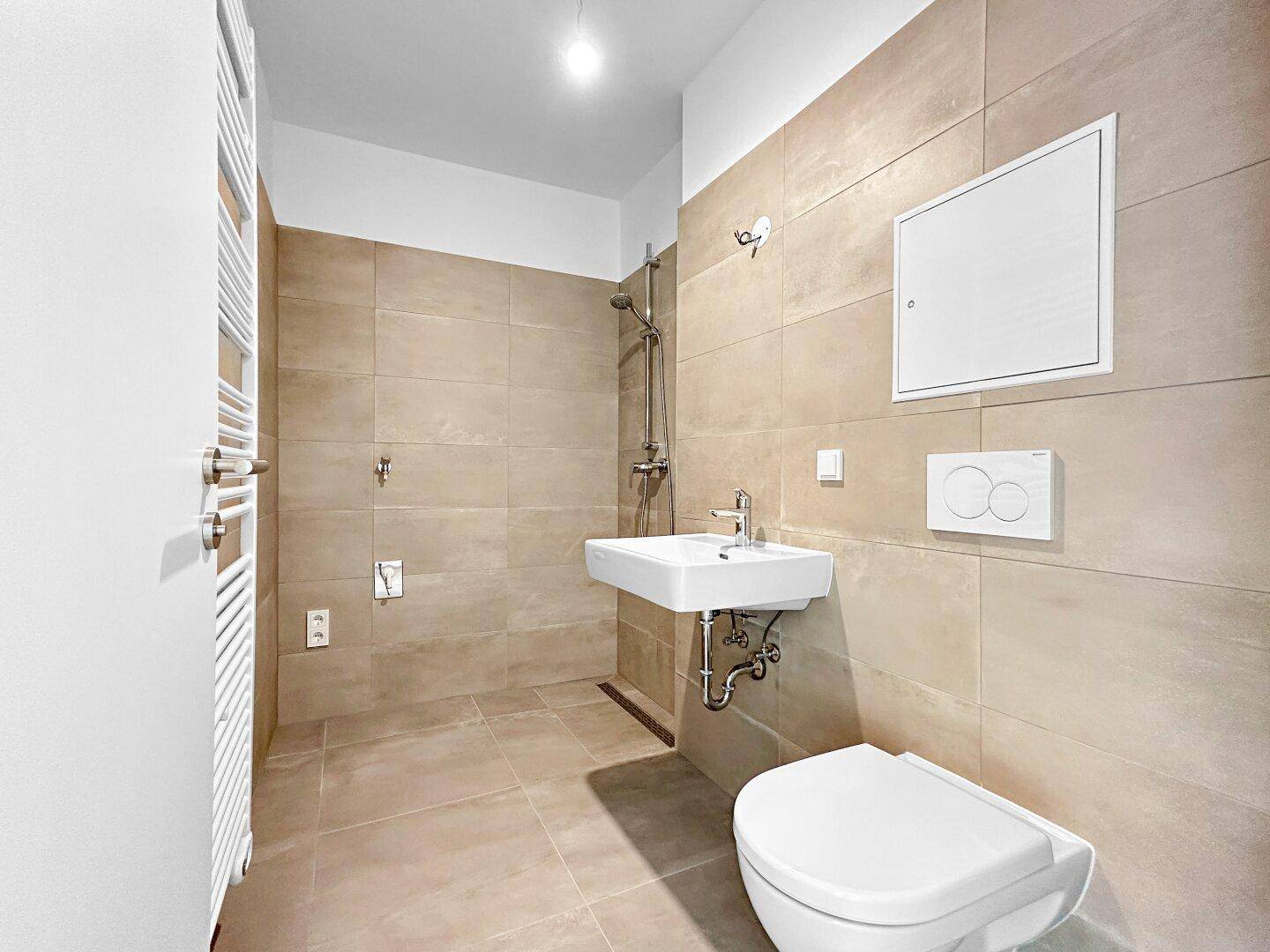 Modernes Badezimmer mit beigefarbenen Fliesen, Dusche, wandhängendem WC und Waschbecken.
