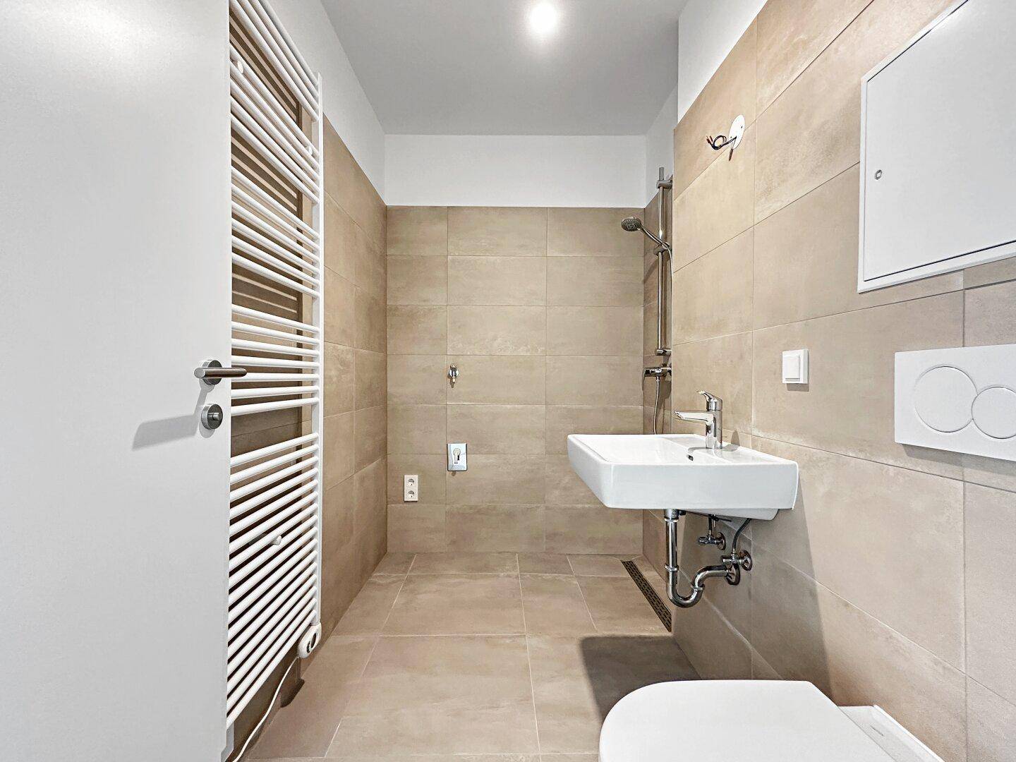 Modernes Badezimmer mit beigefarbenen Fliesen, Dusche, Waschbecken und beheiztem Handtuchhalter.