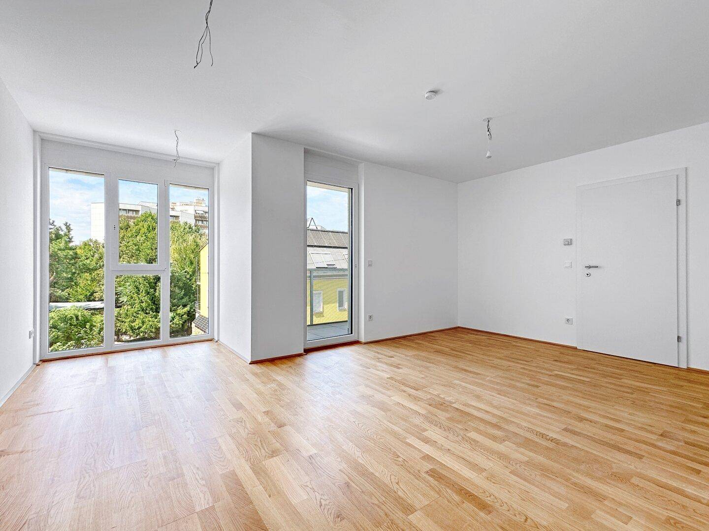Geräumiges, helles Wohnzimmer mit Parkettboden und Zugang zu einem Außenbereich.