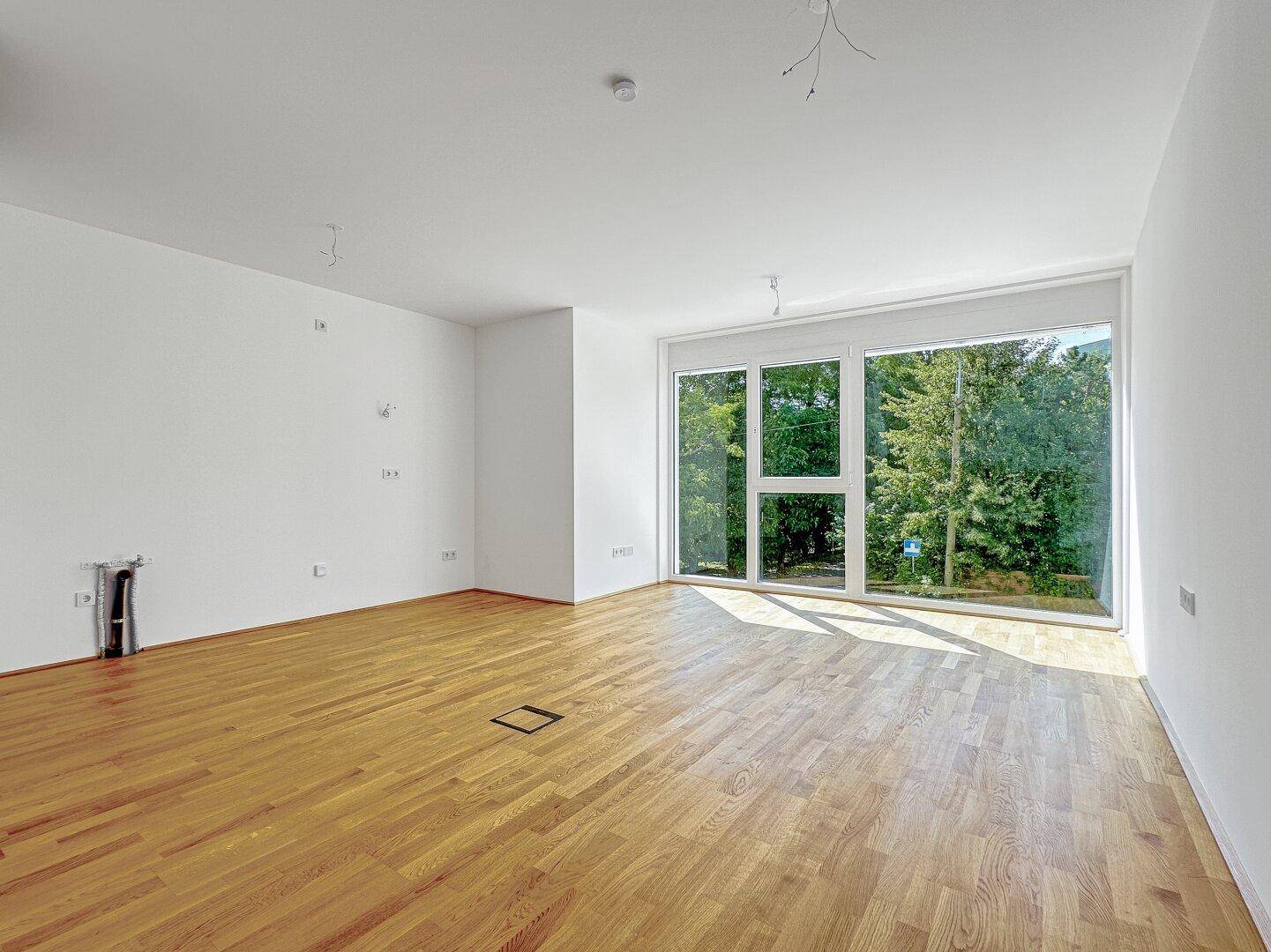 Geräumiges Wohnzimmer mit Parkettboden und bodentiefen Fenstern, die viel Tageslicht hereinlassen.