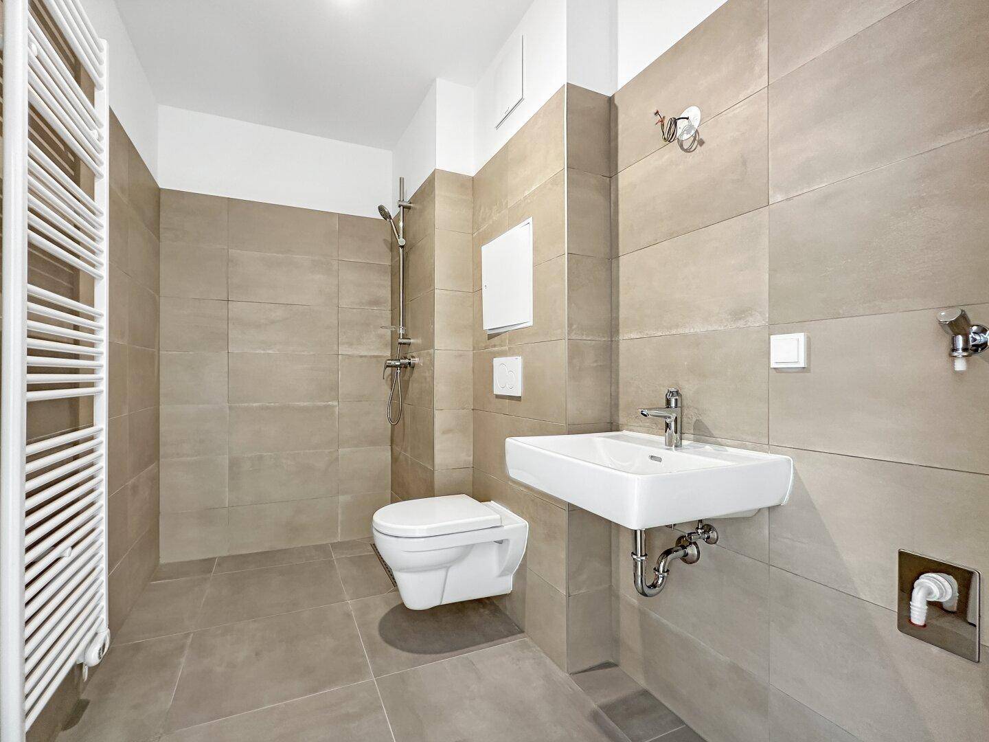 Modernes Badezimmer mit beigefarbenen Fliesen, wandhängendem WC, Waschbecken und Duschbereich.