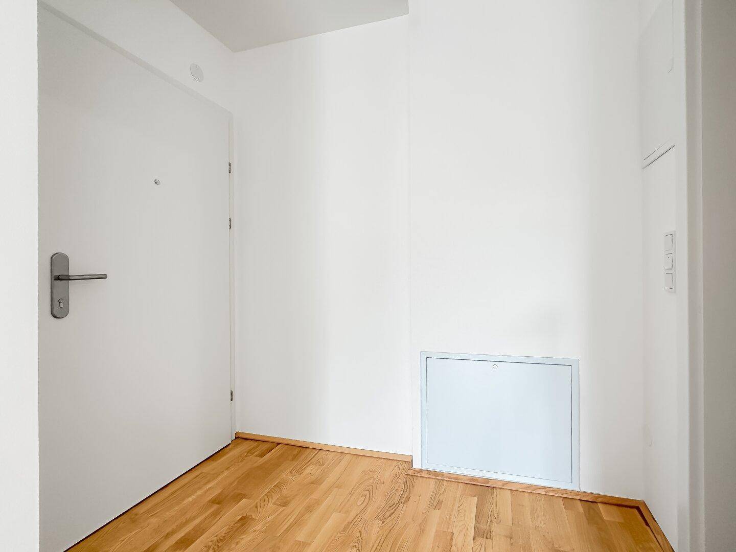 Heller Eingangsbereich mit weißer Tür, Holzfußboden und Zugang zu den Wohnräumen.
