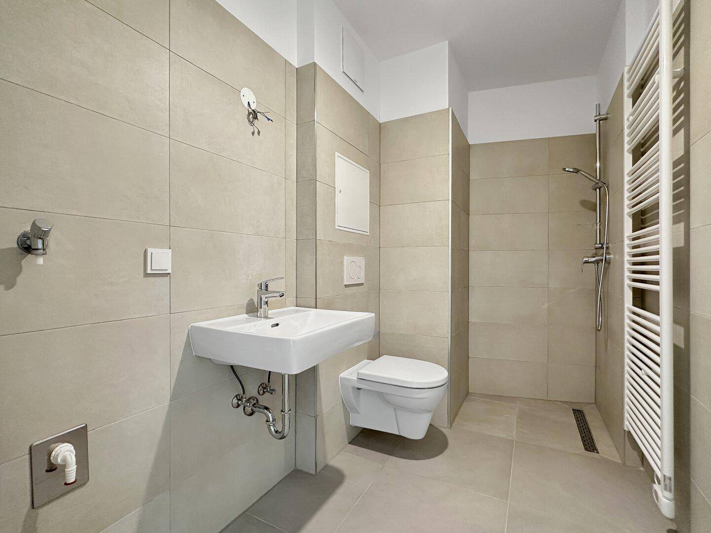 Modernes Badezimmer mit beigefarbenen Fliesen, wandhängendem WC, Waschbecken und ebenerdiger Dusche.