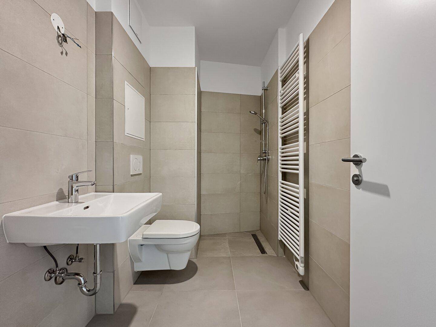 Modernes Badezimmer mit beigefarbenen Fliesen, ebenerdiger Dusche und praktischem Handtuchheizkörper.