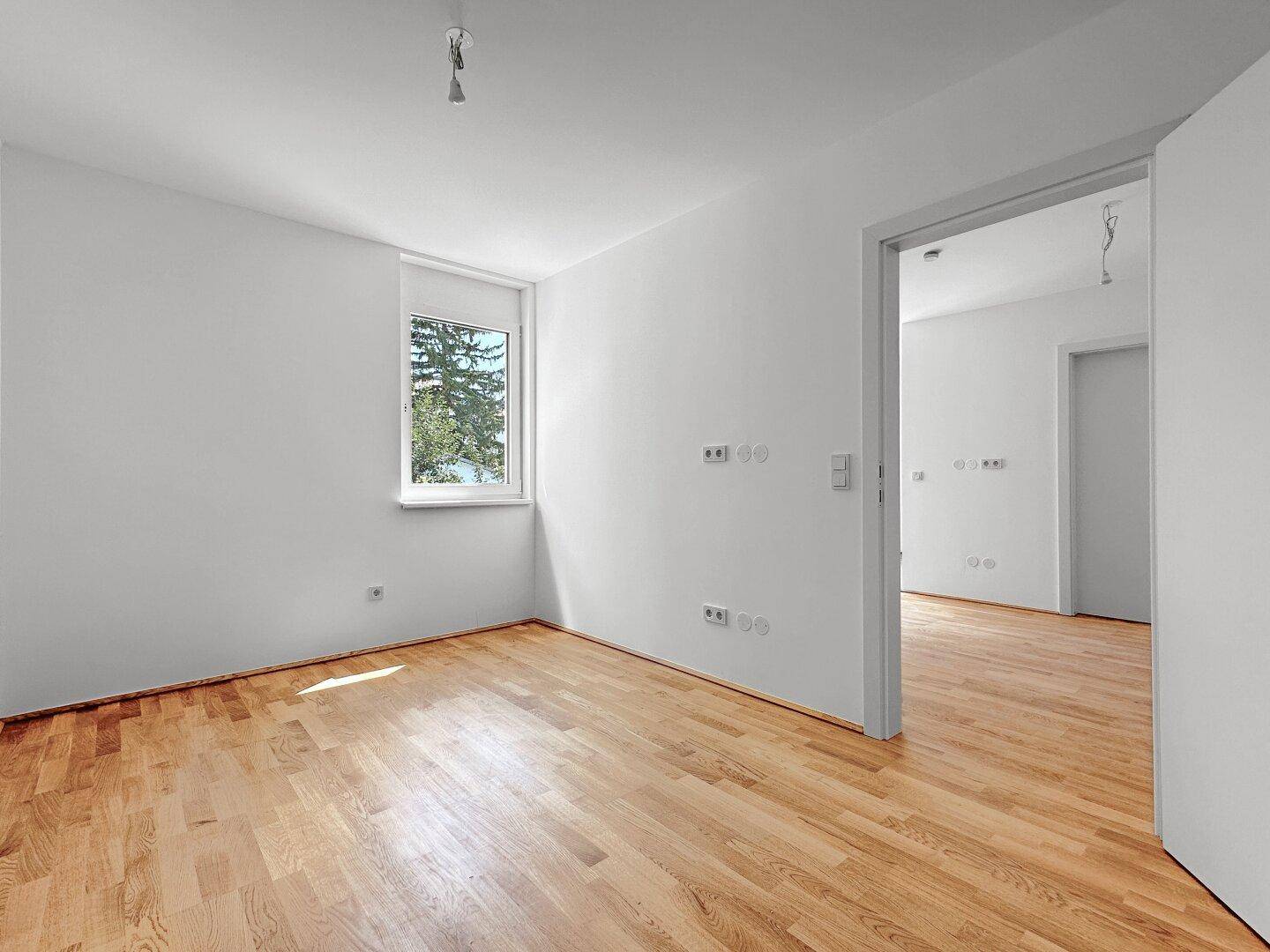 Heller Raum mit Holzboden und Fenster, bietet einen ruhigen Blick ins Grüne.