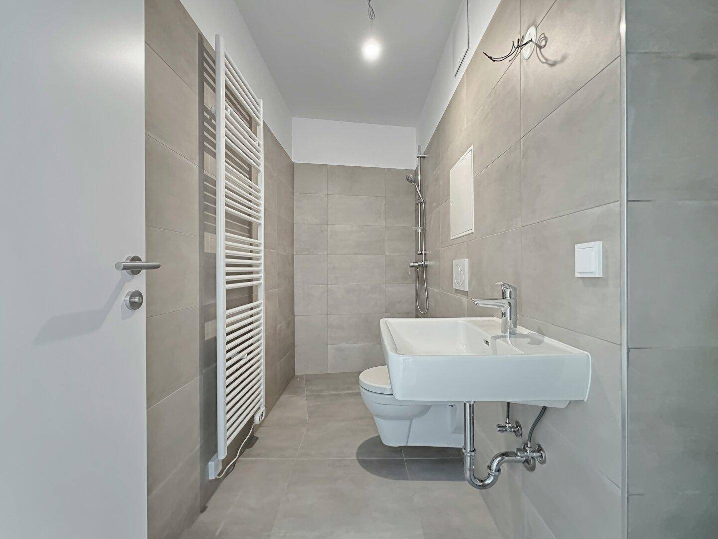 Modernes Badezimmer mit grauen Fliesen, Dusche und beheiztem Handtuchhalter.
