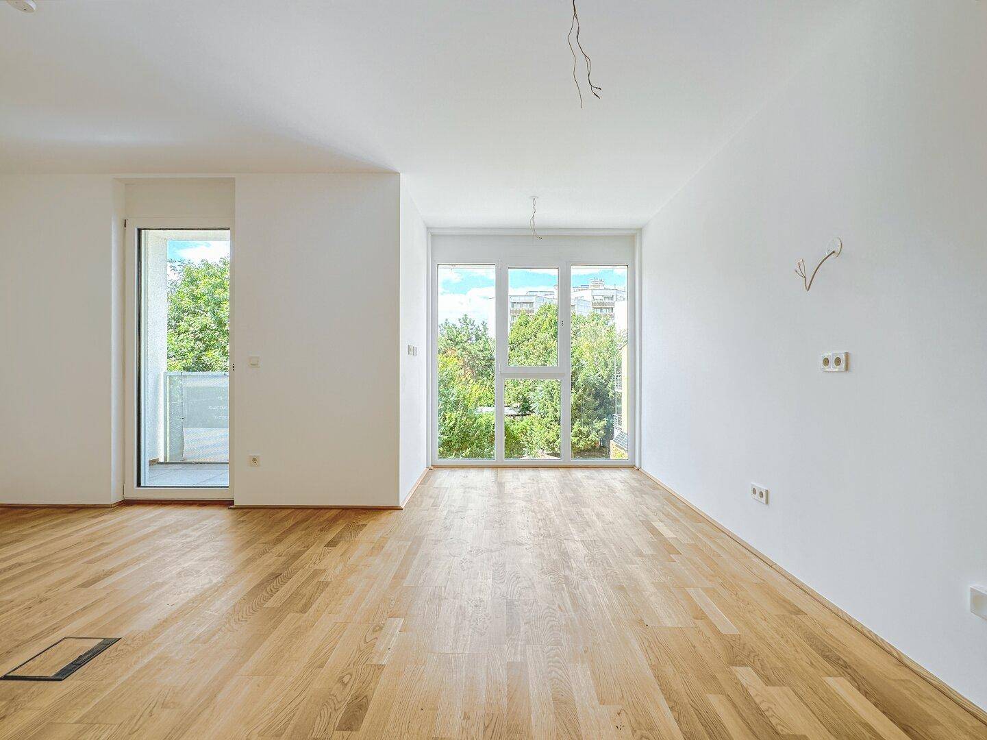 Geräumiges, helles Zimmer mit Parkettboden und weitem Blick ins Grüne durch große Fenster.