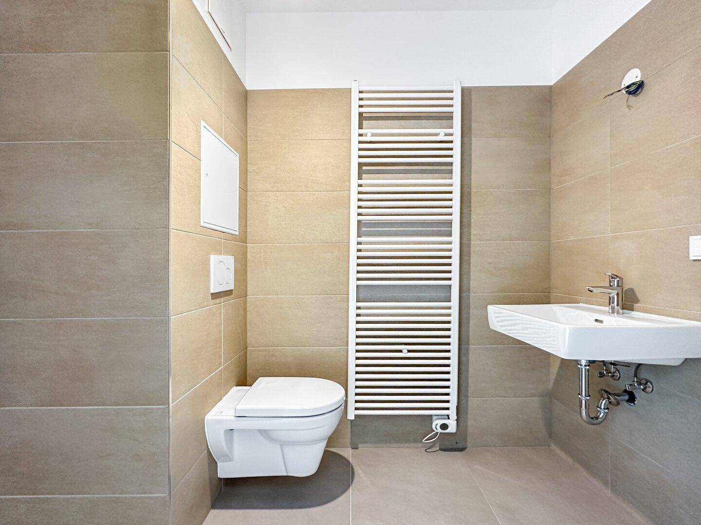 Modernes Badezimmer mit beigefarbenen Fliesen, wandhängendem WC und beheiztem Handtuchhalter.