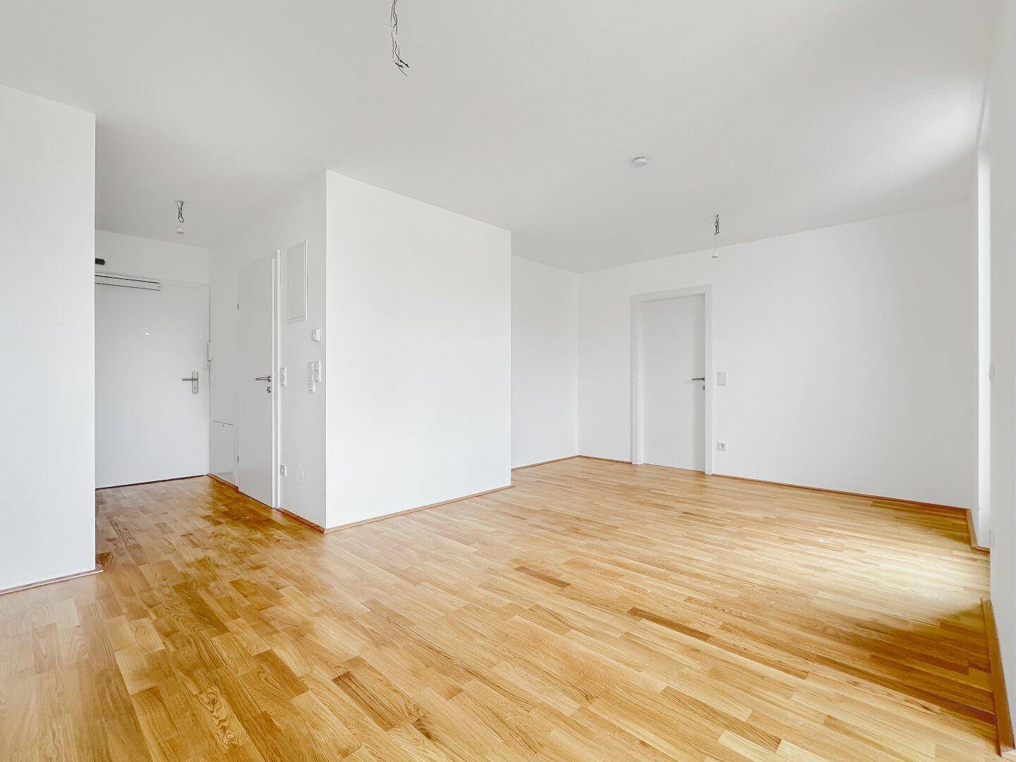 Geräumiger, heller Raum mit Holzboden und weißen Wänden, bietet mehrere Türen zu angrenzenden Bereichen.