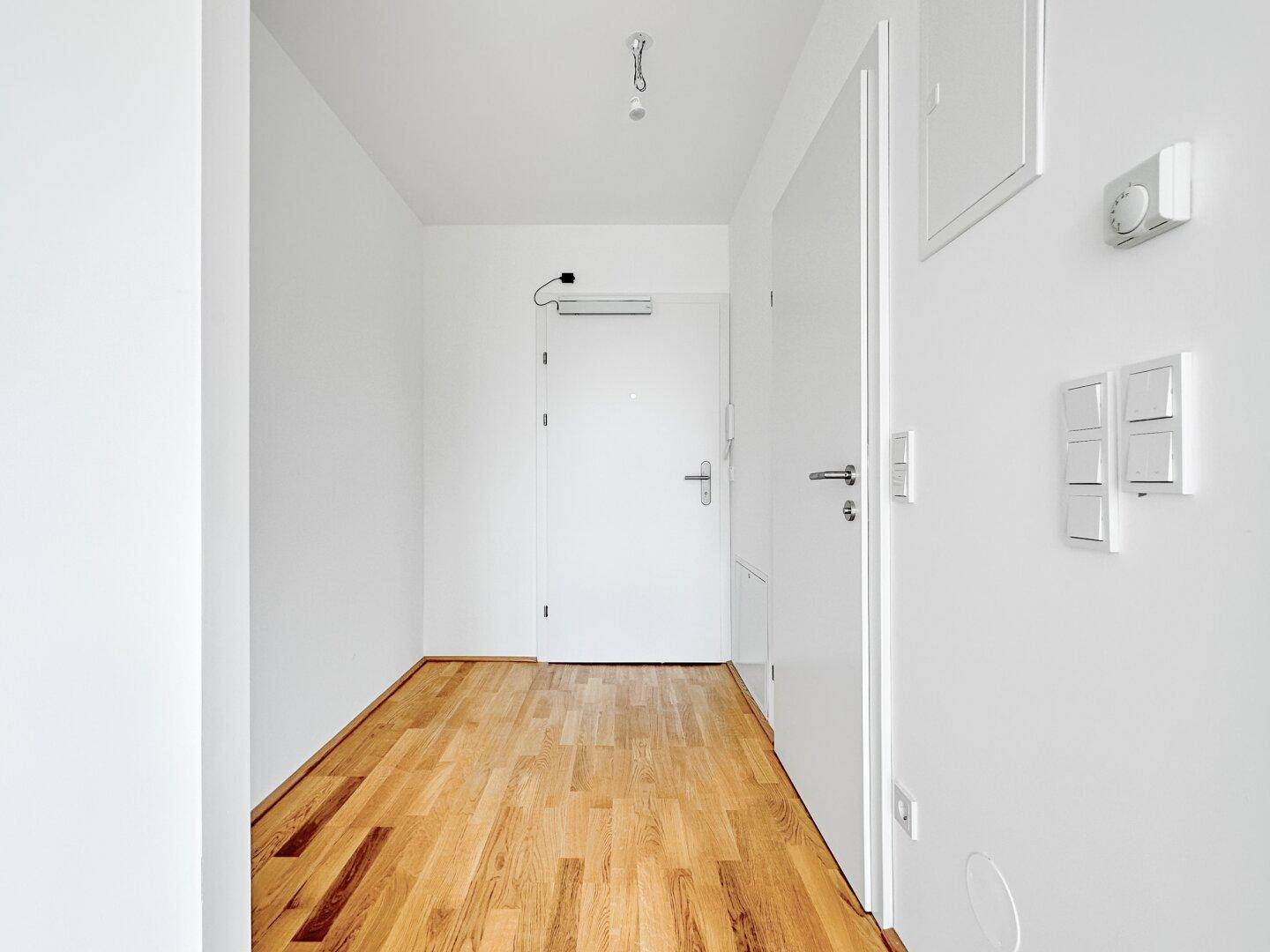 Heller Eingangsbereich mit Holzboden, weiß gestrichenen Wänden und der Haupttür zur Wohnung.