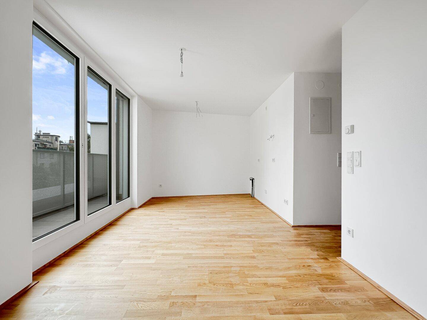 Geräumiger, heller Innenraum mit Holzboden und bodentiefen Fenstern, die viel Tageslicht hereinlassen.