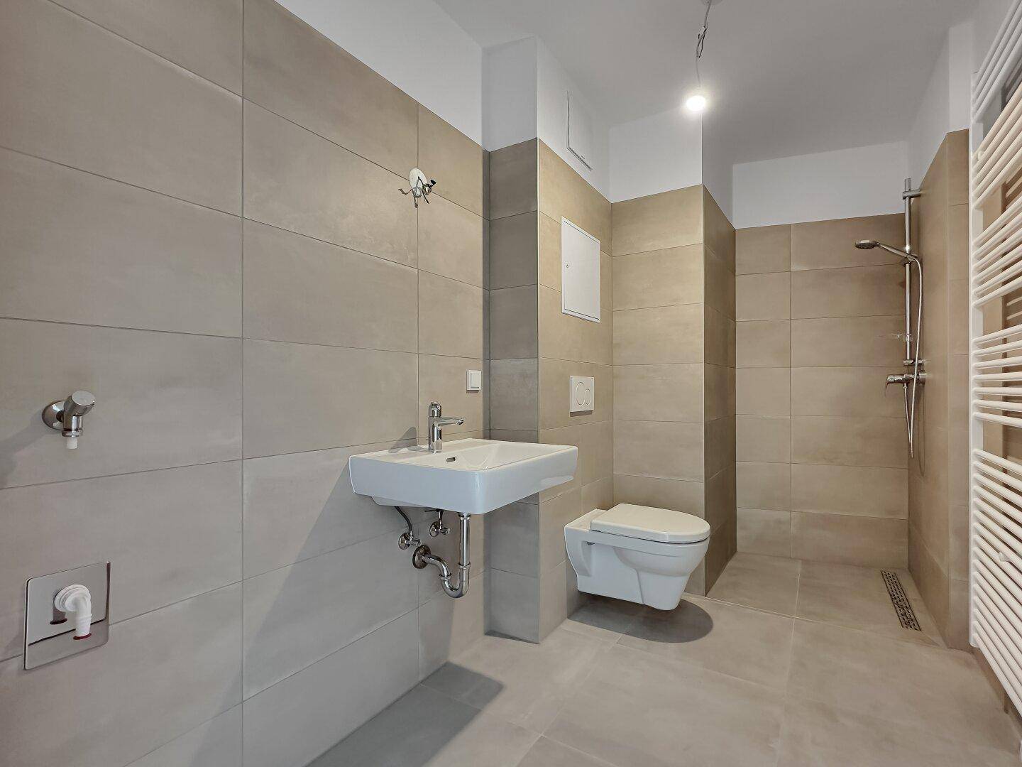 Modernes Badezimmer mit beigefarbenen Fliesen, wandhängendem WC, Waschbecken und ebenerdiger Dusche.