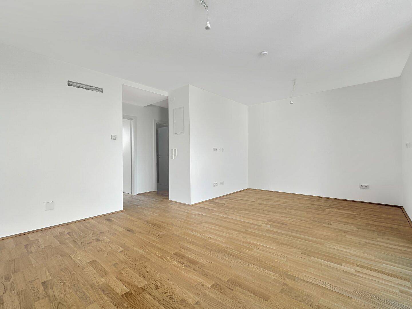 Helles, leeres Zimmer mit Holzboden und weißen Wänden, bereit zur individuellen Gestaltung.