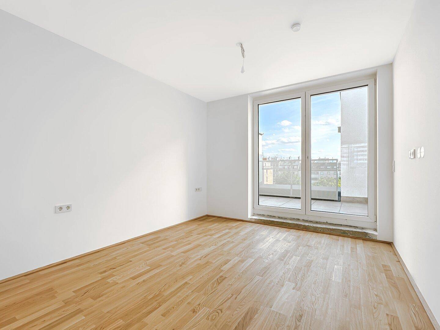 Lichtdurchflutetes Zimmer mit Holzboden und Zugang zu einem Balkon, bietet eine helle Atmosphäre.