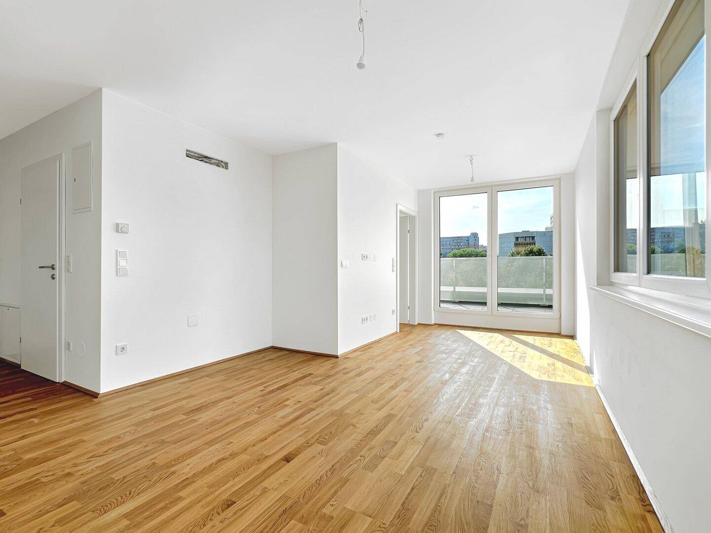 Geräumiges, helles Zimmer mit Holzboden und Zugang zu einem Balkon mit Stadtblick.