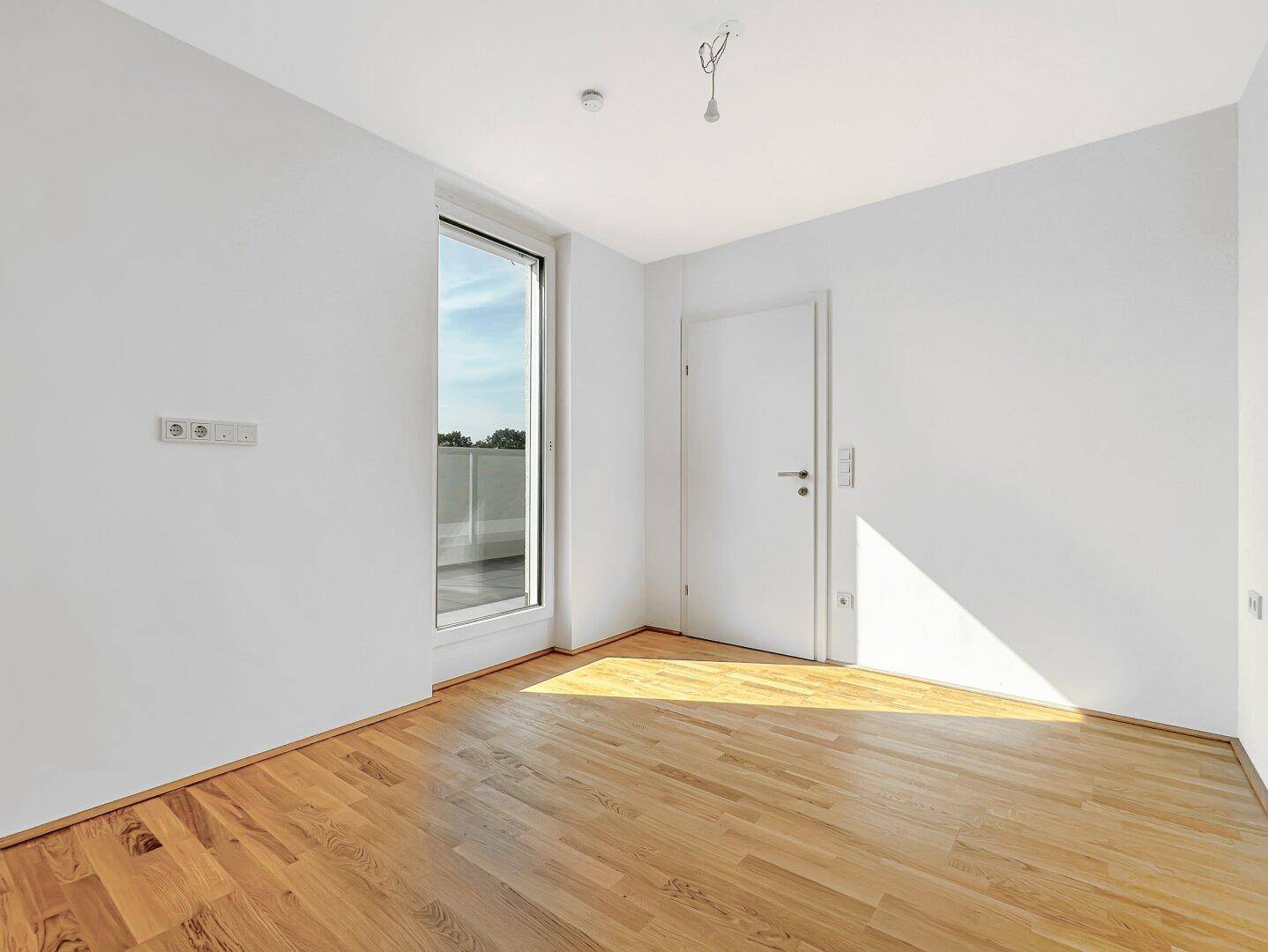 Helles Schlafzimmer mit Holzboden und Fenster mit Zugang zu einem Balkon.