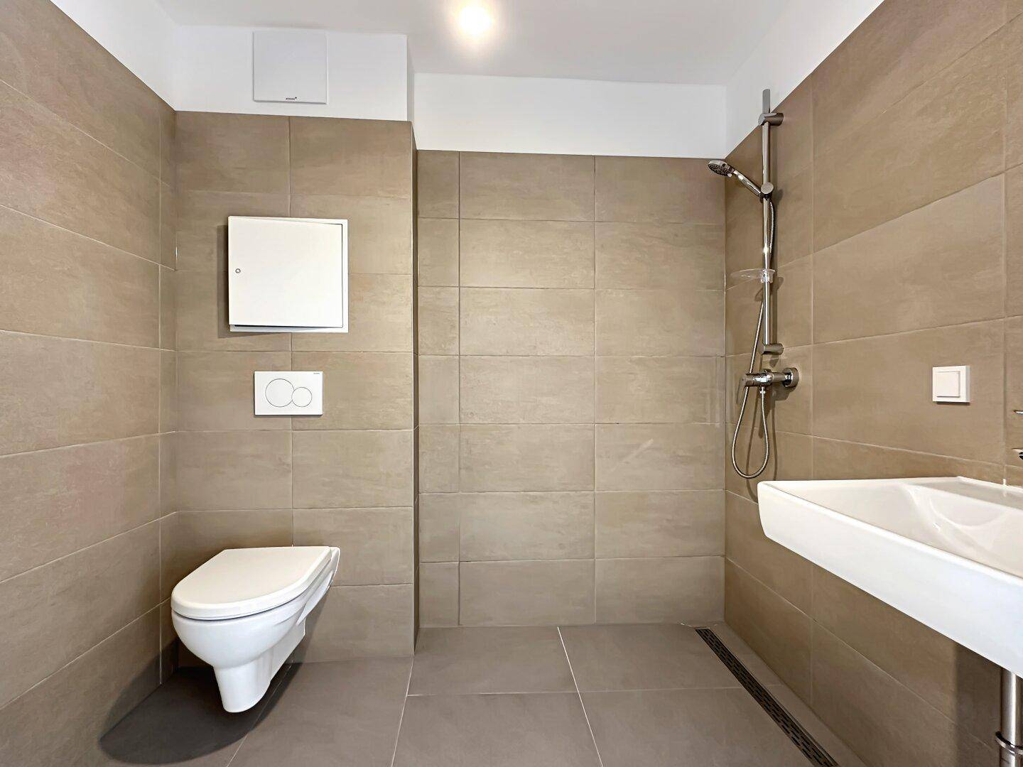 Modernes Badezimmer mit beigefarbenen Fliesen, wandhängendem WC und ebenerdiger Dusche.