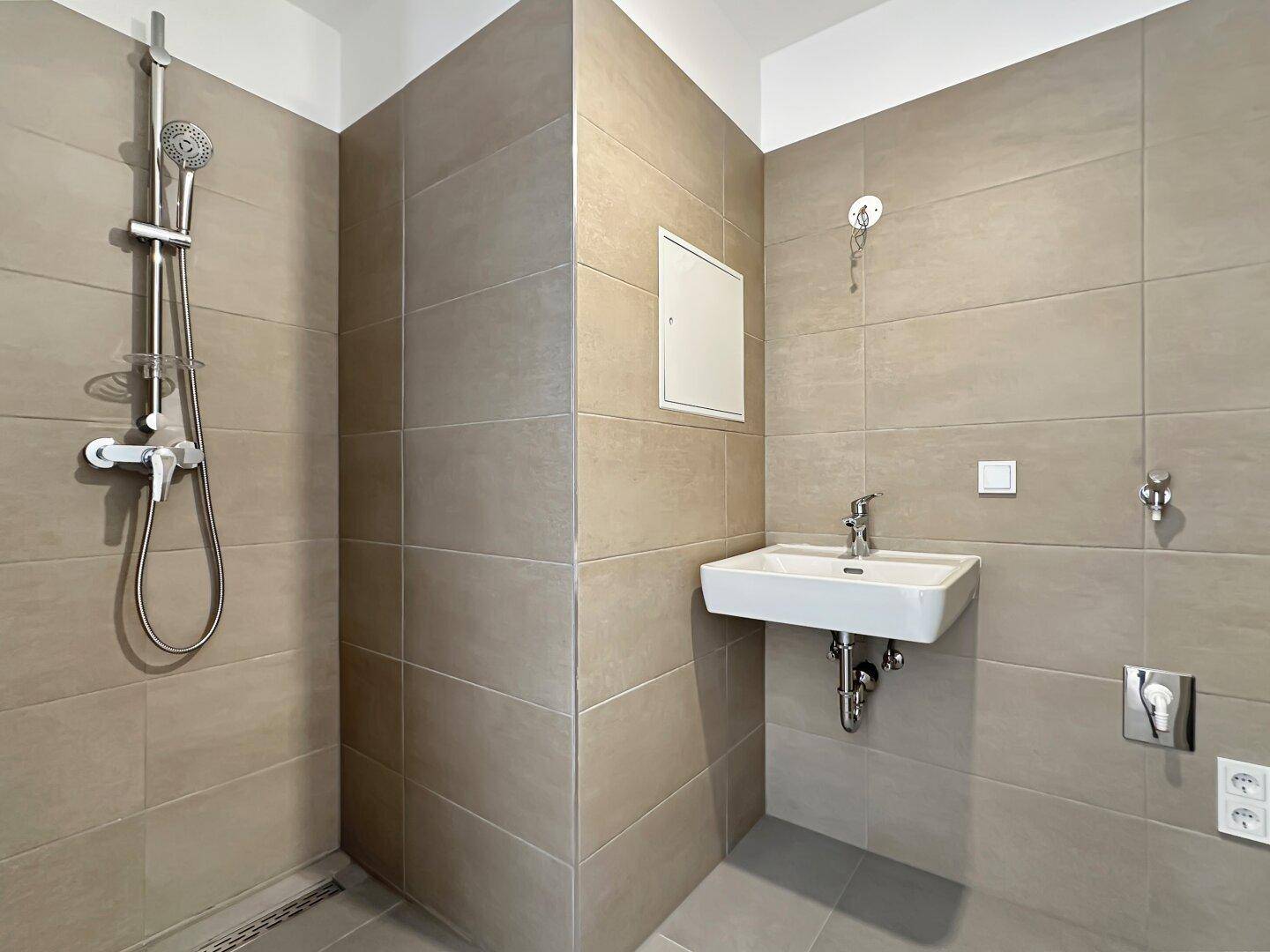 Modernes Badezimmer mit beigefarbenen Fliesen, Dusche und Waschbecken.