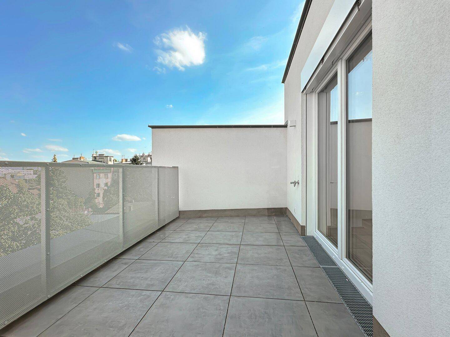Geräumige Terrasse mit grauen Fliesen und moderner Metallbrüstung unter blauem Himmel.