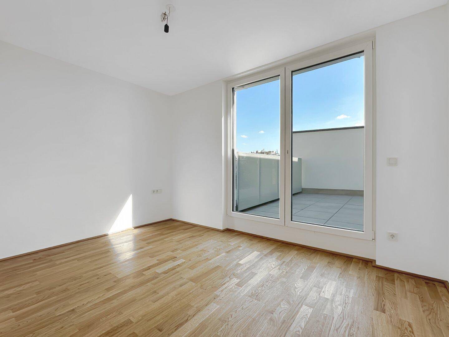 Lichtdurchflutetes Zimmer mit Holzboden und großem Fenster mit Zugang zu einem Außenbereich.