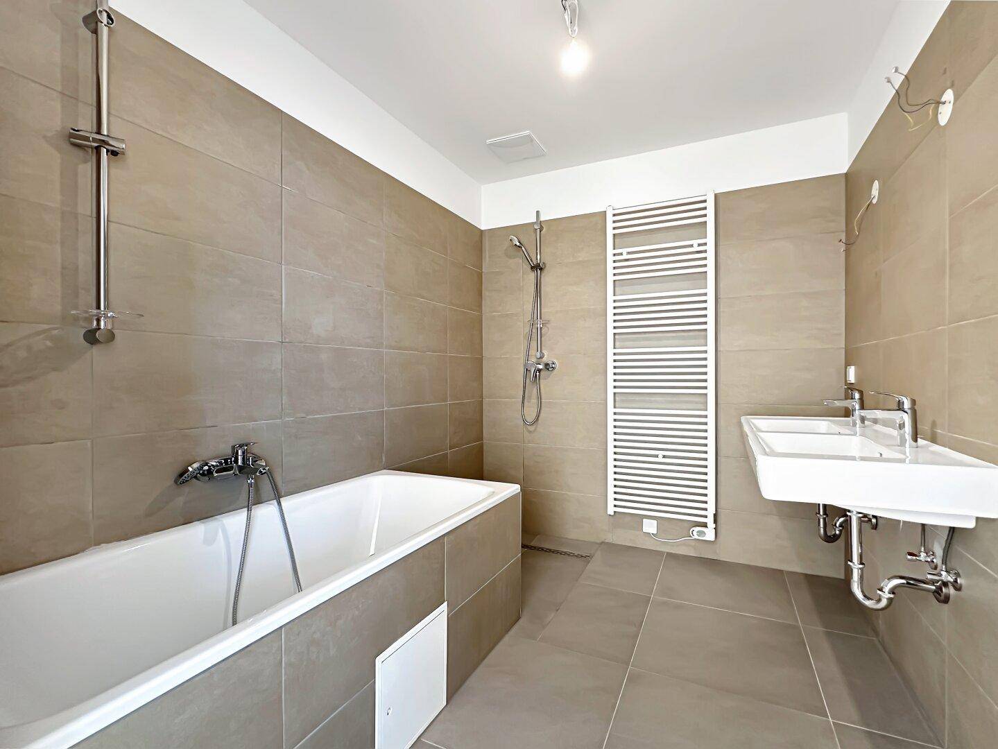 Modernes Badezimmer mit beigefarbenen Fliesen, Badewanne, Dusche und beheiztem Handtuchhalter.