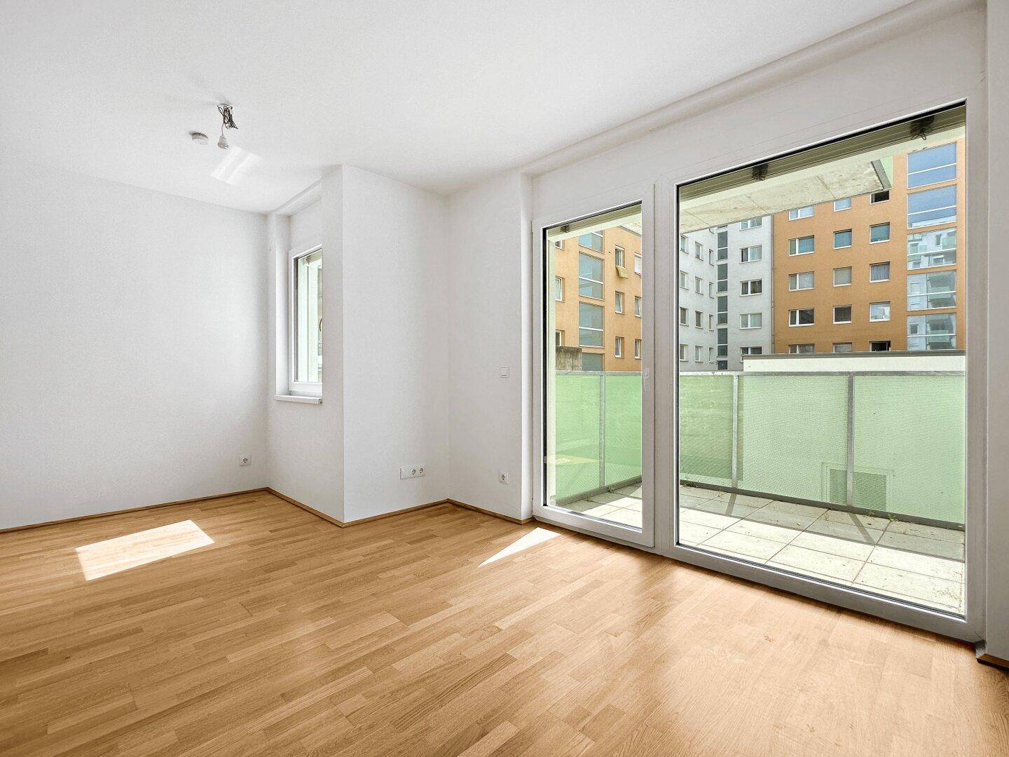 Geräumiger, heller Wohnbereich mit Holzboden und großen Fenstern mit Blick auf die Stadt.
