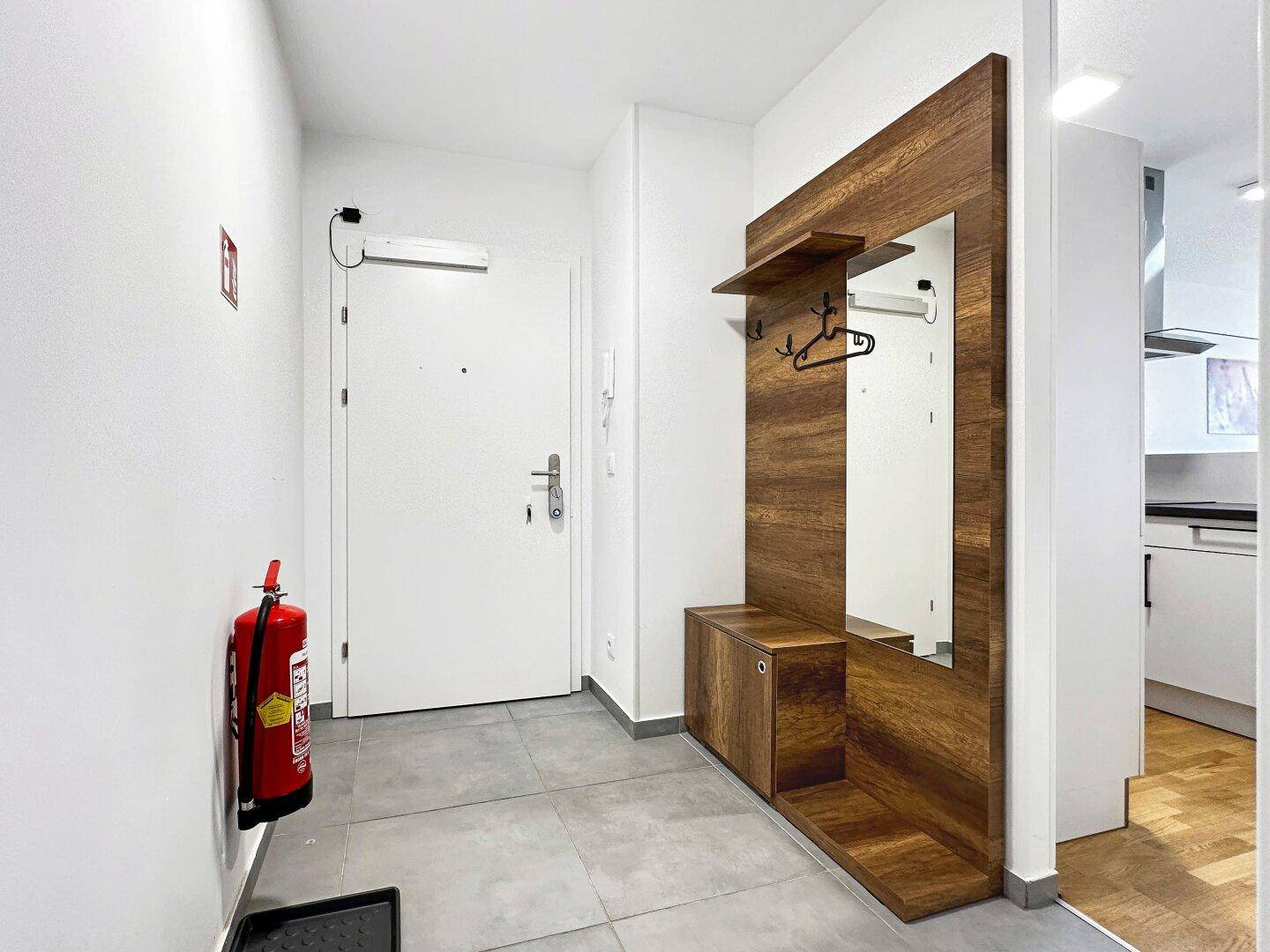 Eingangsbereich mit modernem Holzpaneel, Spiegel und Garderobe, sowie Fliesenboden.