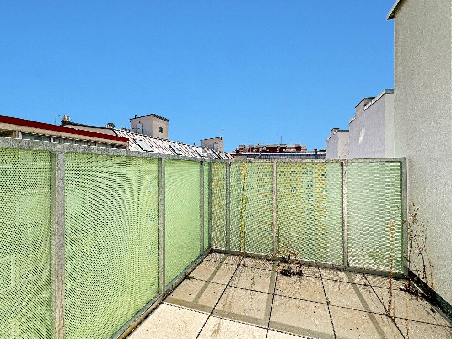 Kleiner Balkon mit grüner Lochblechverkleidung und Blick auf umliegende Gebäude.
