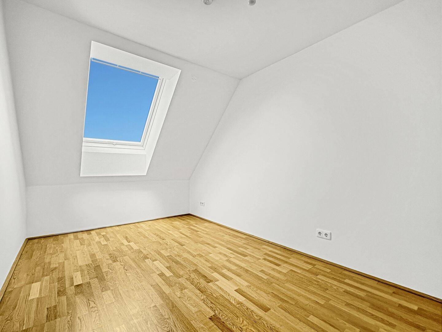 Helles Zimmer mit Holzboden und einem großen Dachfenster, ideal als Schlaf- oder Arbeitszimmer.