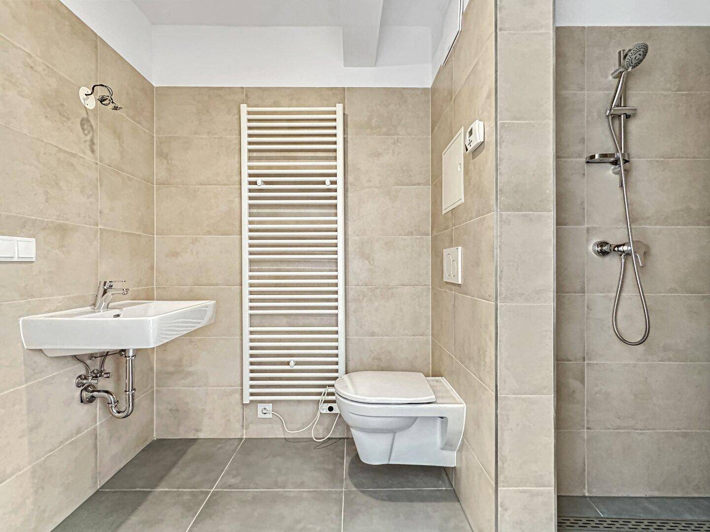 Modernes Badezimmer mit beigefarbenen Fliesen, Dusche, WC und beheiztem Handtuchhalter.