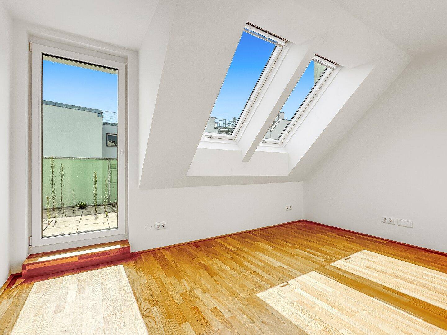 Heller Raum im Dachgeschoss mit Holzboden, Dachfenstern und Zugang zu einer privaten Terrasse.
