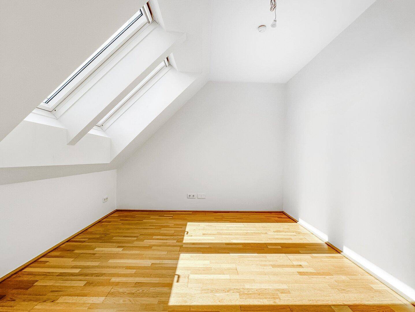 Dachgeschosszimmer mit Holzboden und zwei großen Dachfenstern, die viel Licht spenden und den Raum erhellen.