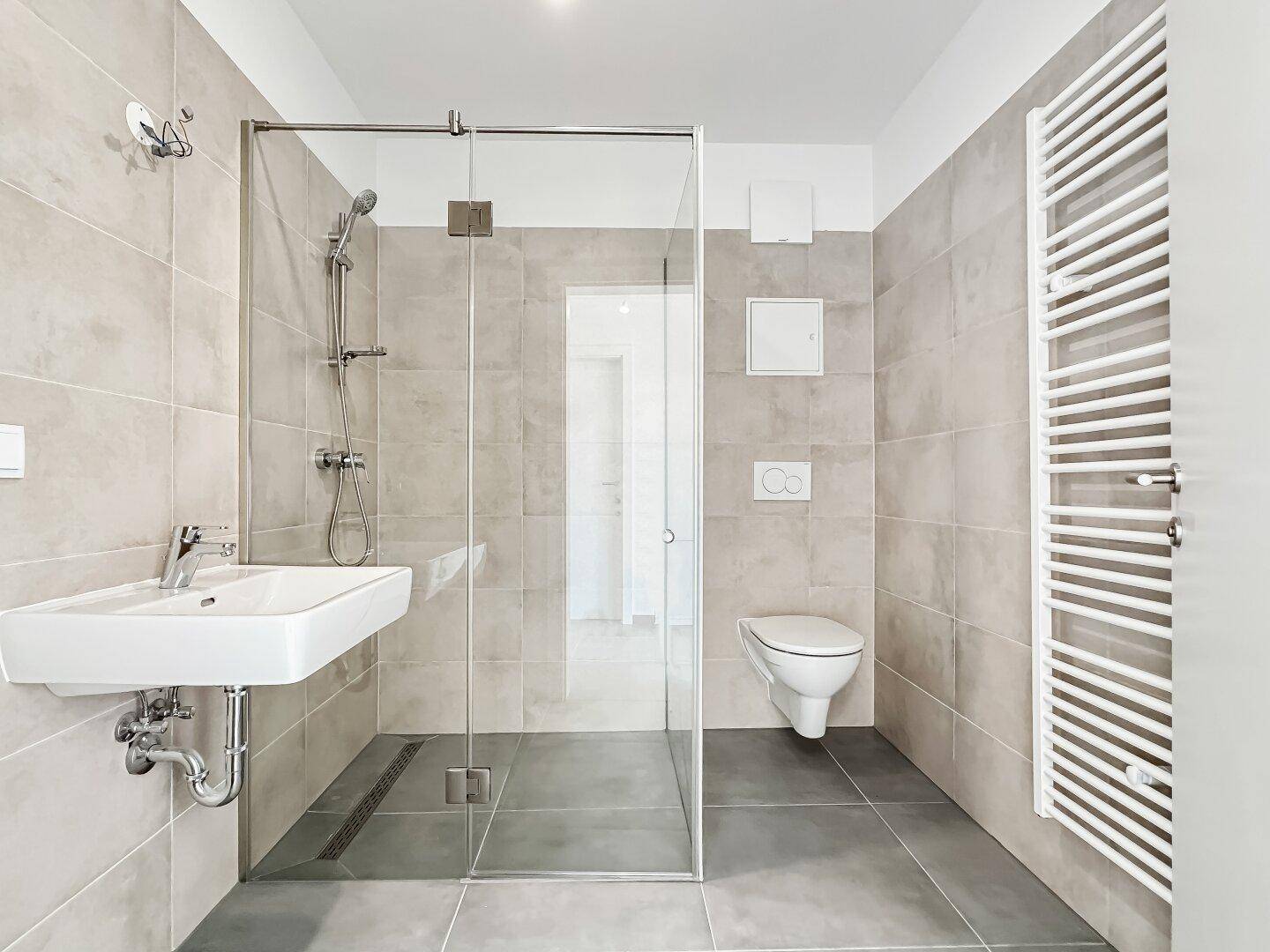 Modernes Badezimmer mit begehbarer Dusche, Wand-WC, Einzelwaschbecken und beheiztem Handtuchhalter in hellen Grautönen.