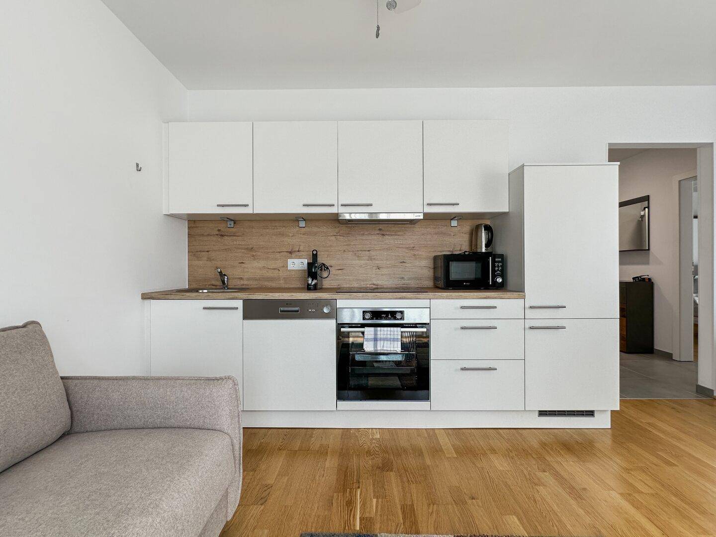 Helle Einbauküche mit weißen Schränken, Holzrückwand und modernen Geräten.