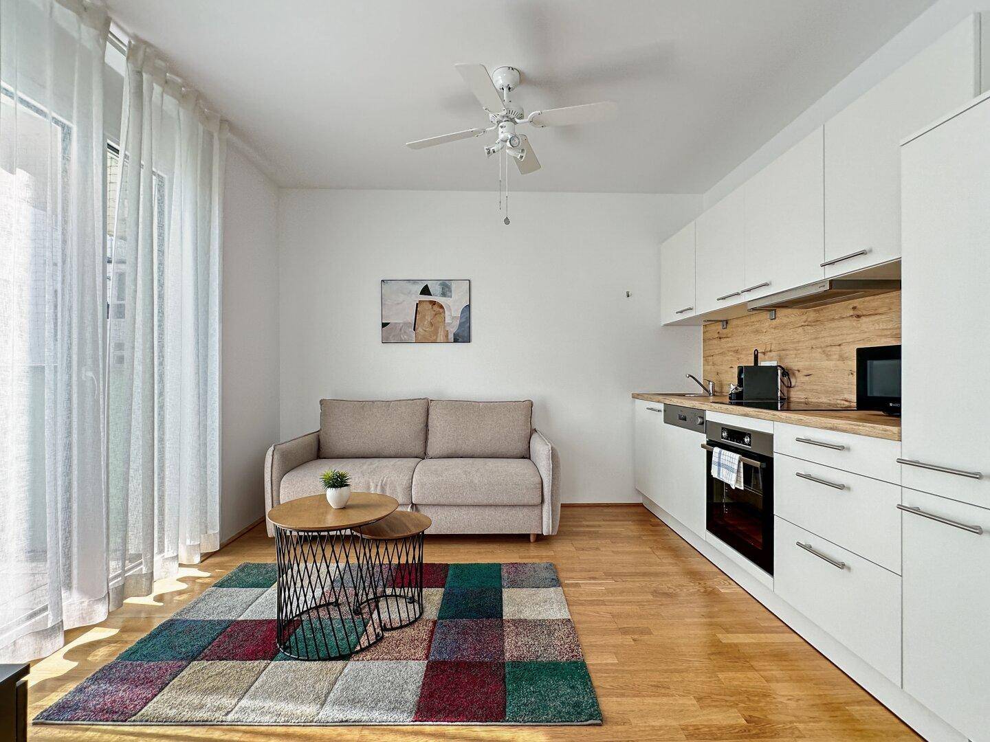 Lichtdurchfluteter Wohnbereich mit Sofa, Teppich und Zugang zu einem Balkon.