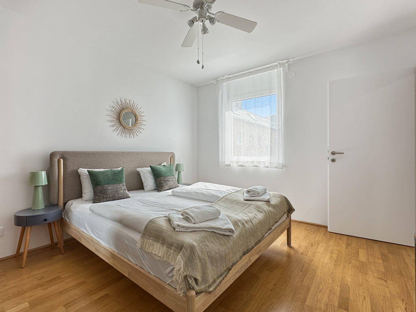 Helles Schlafzimmer mit großem Fenster, Doppelbett und Nachttischen.