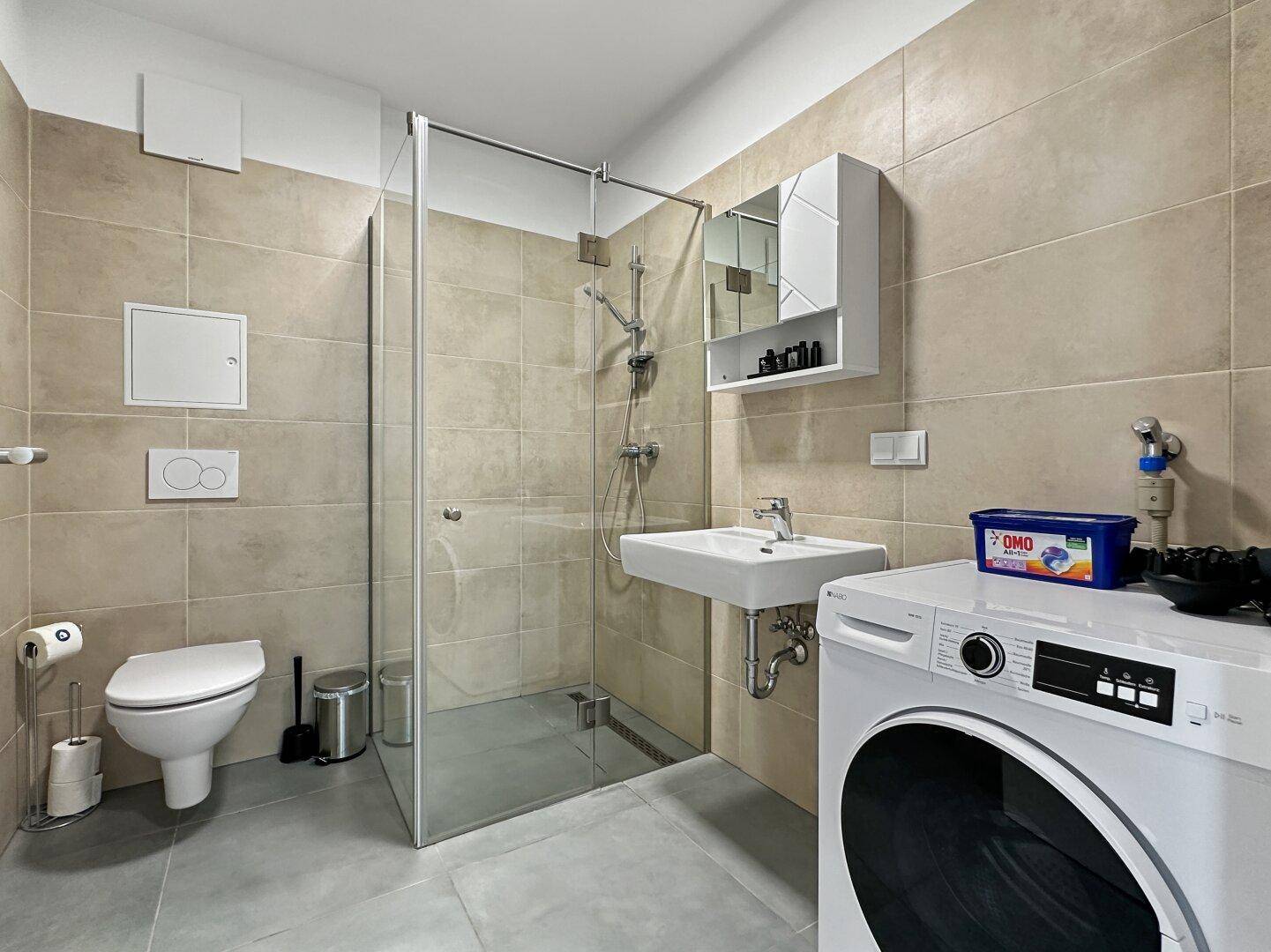 Modernes Badezimmer mit begehbarer Dusche, WC, Waschbecken und Waschmaschine.