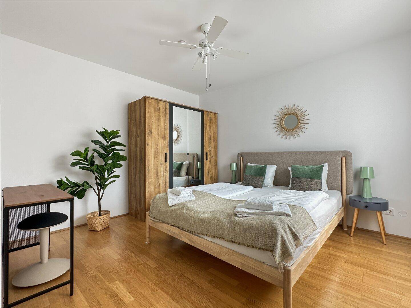 Gemütliches Schlafzimmer mit Holzboden, großem Bett, Kleiderschrank und Deckenventilator.