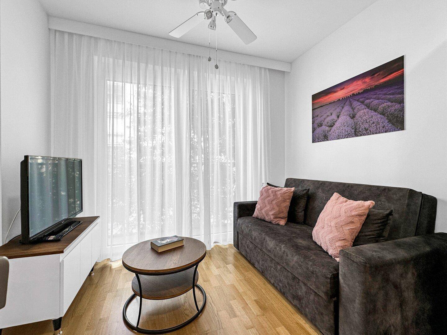 Gemütliches Wohnzimmer mit Sofa, Couchtisch und großem Fenster mit Zugang zu einem Balkon.