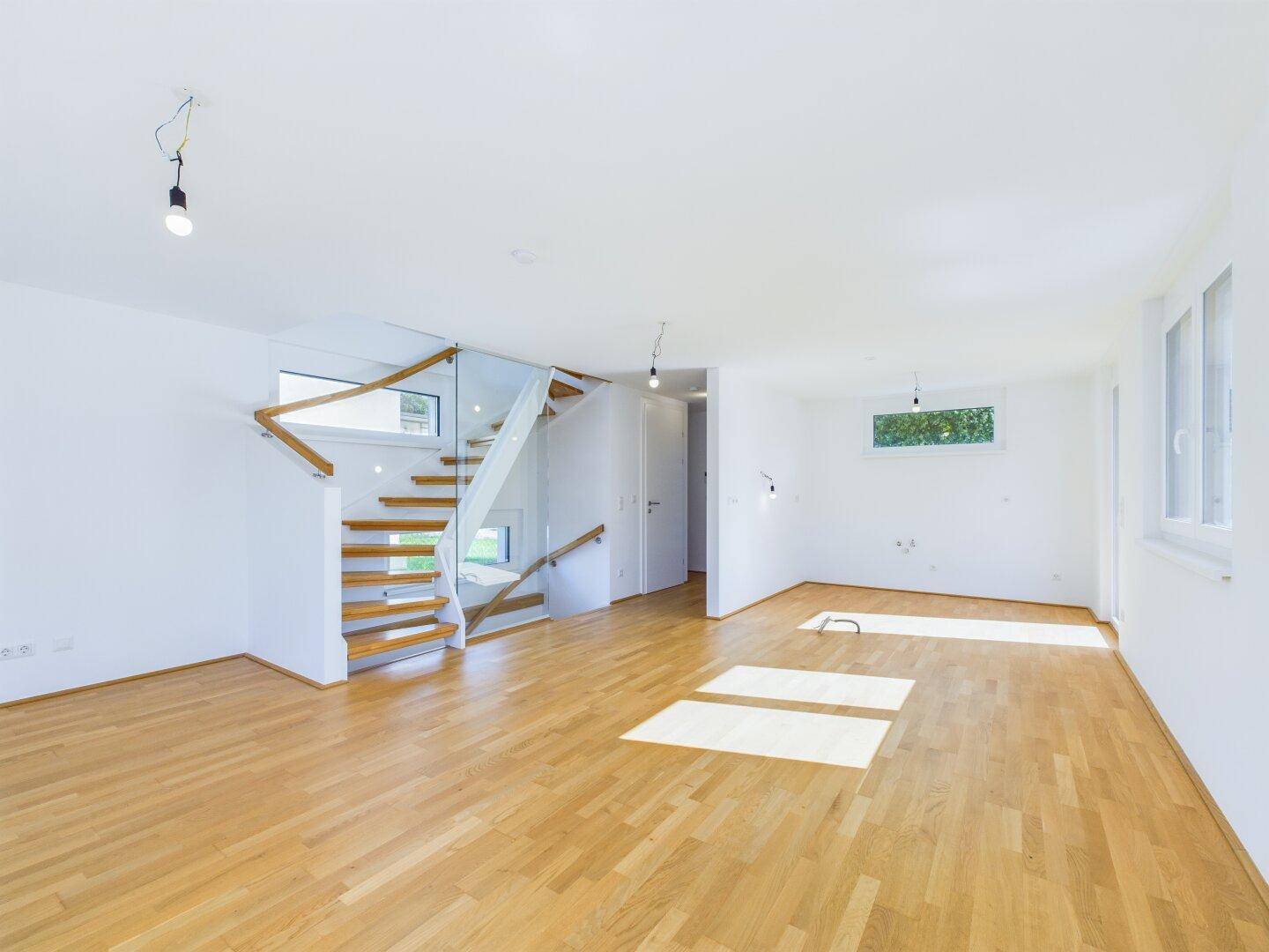 Heller, offener Wohnbereich mit Holzparkettboden und moderner Treppe mit Glasgeländer.