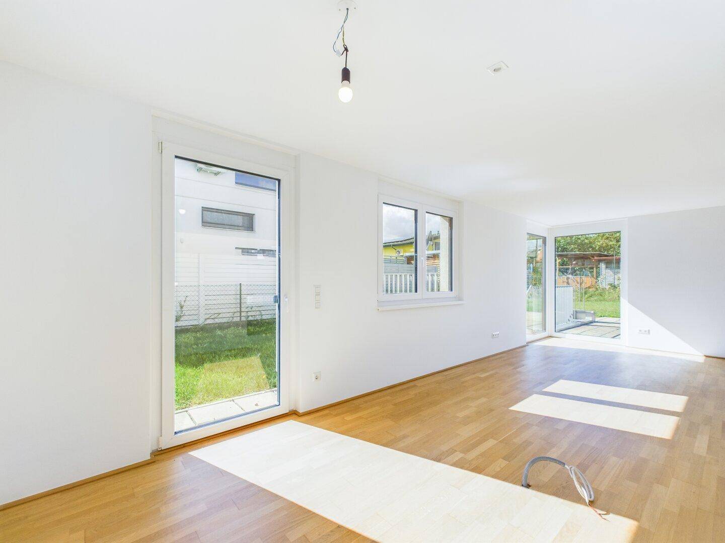 Lichtdurchfluteter Wohnraum mit Holzboden und direktem Zugang zum Garten durch große Fenstertüren.