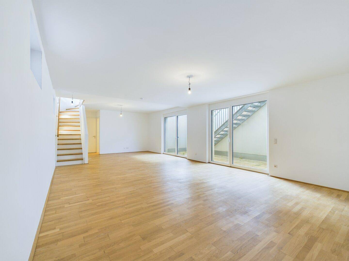 Geräumiger Wohnbereich mit Holzboden und Zugang zu einem Außenbereich über große Glastüren.