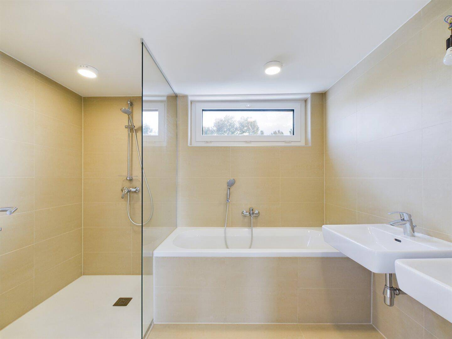Modernes Badezimmer mit Badewanne, ebenerdiger Dusche und Fenster für natürliche Belüftung.