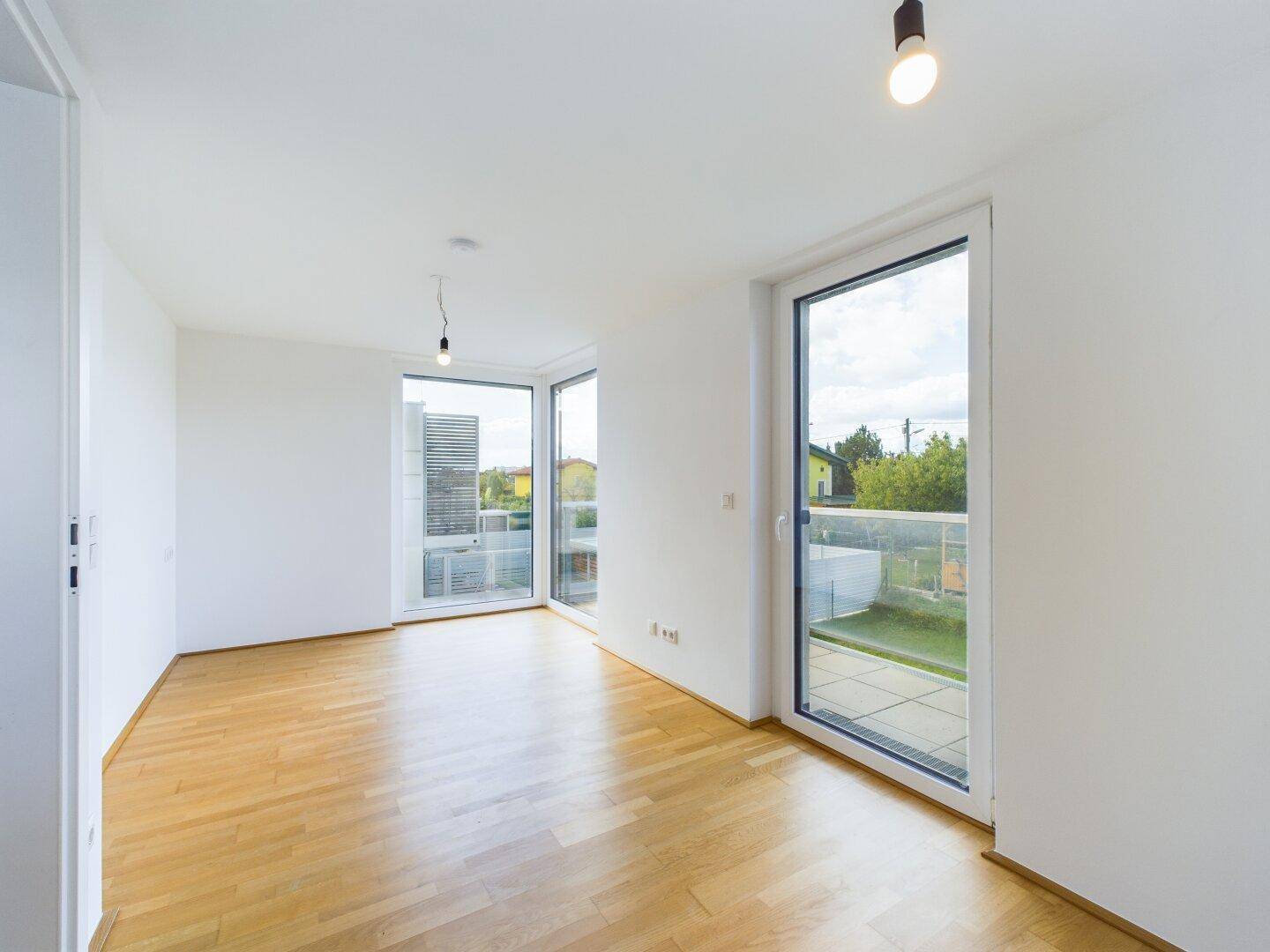 Helles Zimmer mit Holzboden und Zugang zu einem Balkon, bietet viel natürliches Licht.