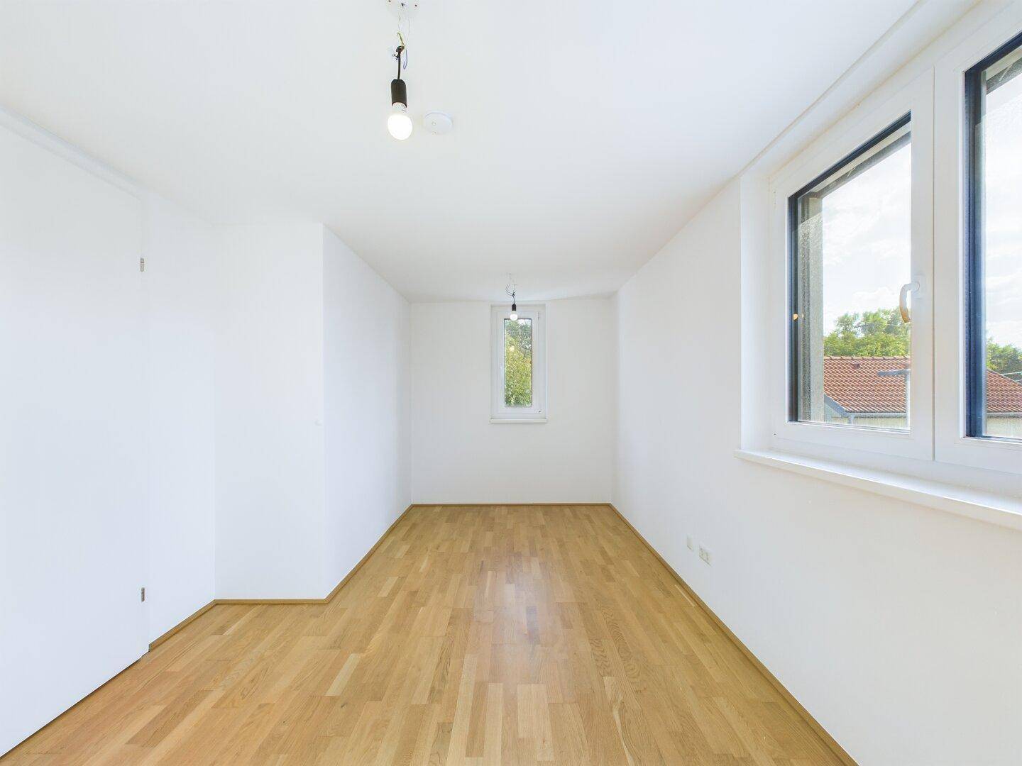 Helles Schlafzimmer mit Holzboden und mehreren Fenstern für viel Tageslicht.